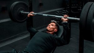 Man performing bench press with heavy barbell in a gym setting, focusing on strength training.